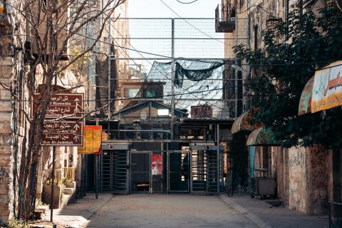A checkpoint across a road in Hebron. It spans the whole road and extends very high, with netting and metal bars.