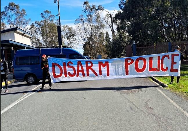 Dos activistas sostienen una gran pancarta blanca que dice "desarmar a la policía".