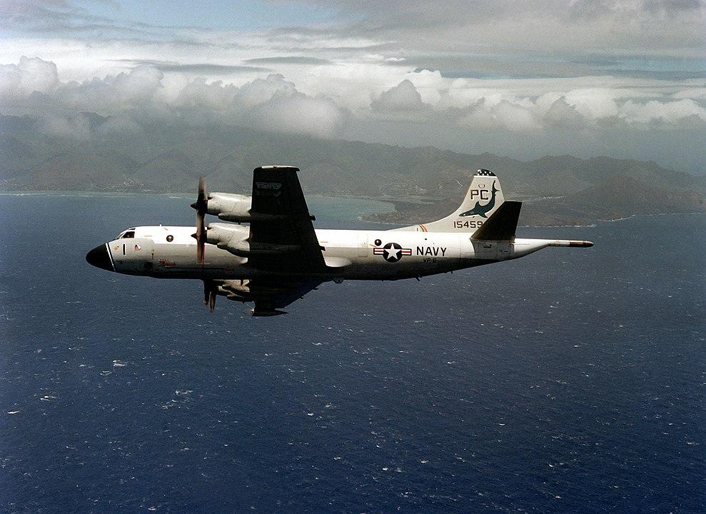 A large military plane in flight over the ocean. It has a US flag and the word "Navy" on the side