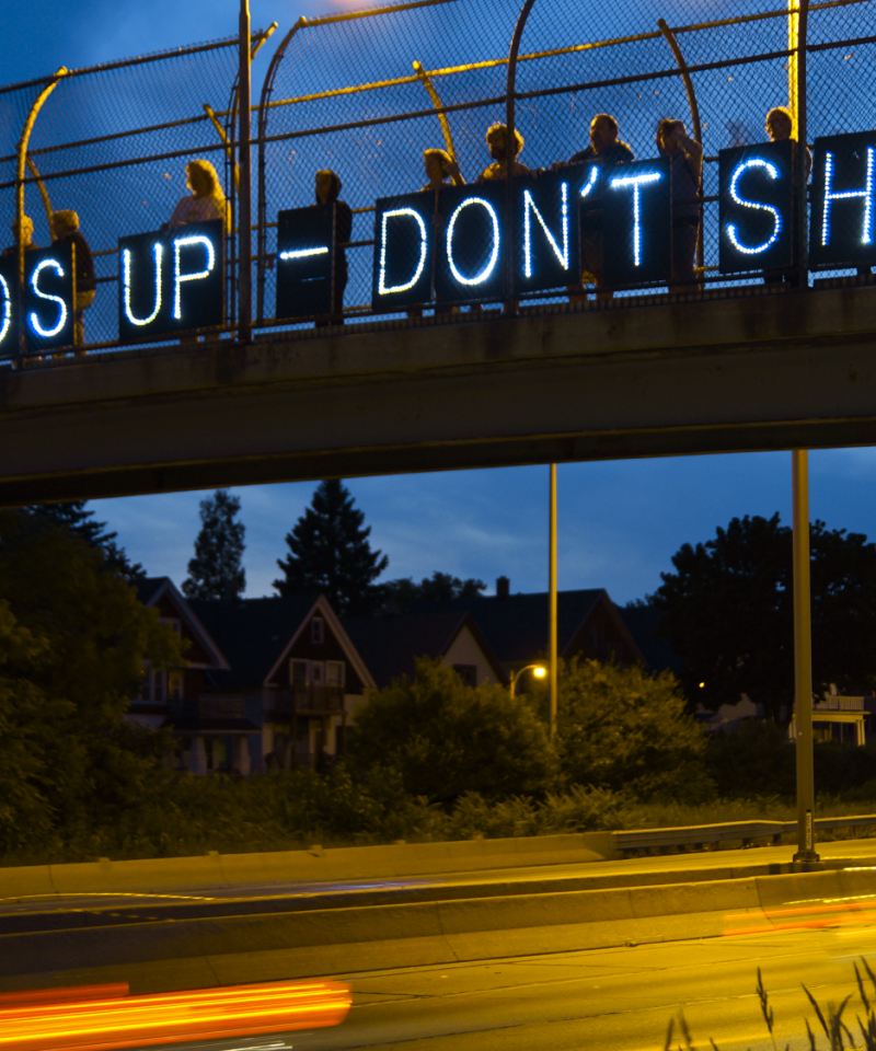 Protesters hold banners with small lights reading "Hands up don't shoot" over a road