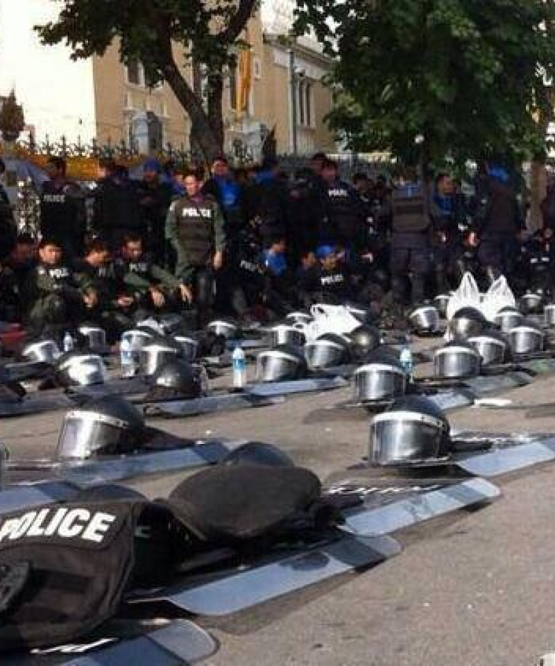 Police stand and sit by the side of the road.  Their shields and helmets are laid out in rows on the road.