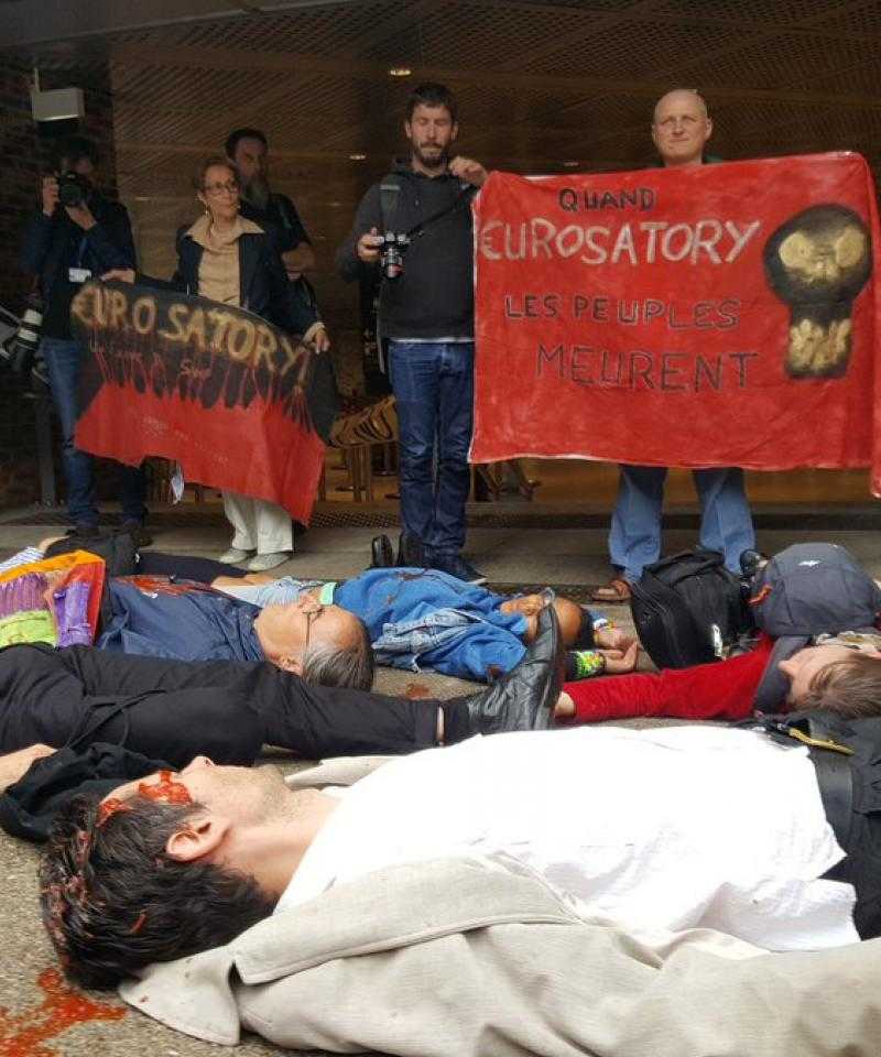 A large group of people lie on the floor in front of banners outside the Eurosatory arms fair