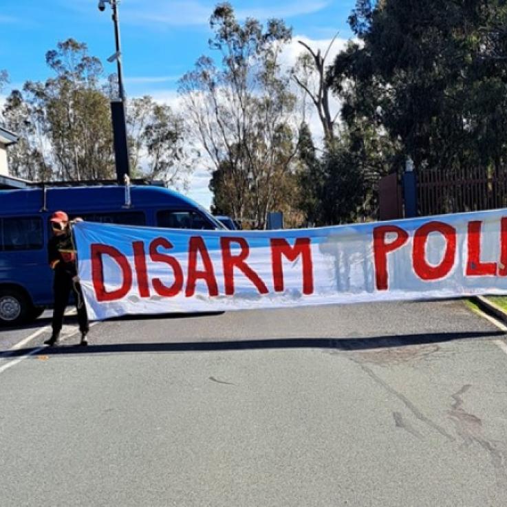 Two activists hold a large white banner reading "disarm police"