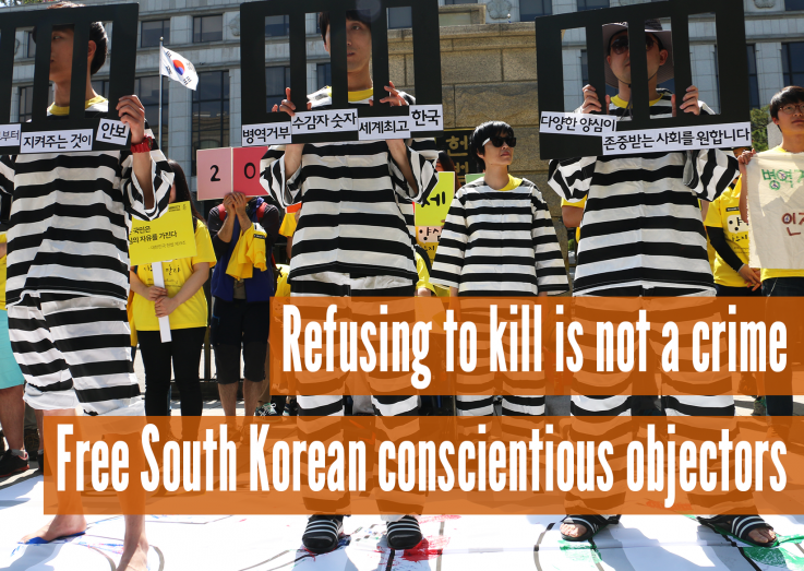 People standing holding signs that look like prison bars, with the text 'Refusing to kill is not a crime, Free South Korean conscientious objectors'