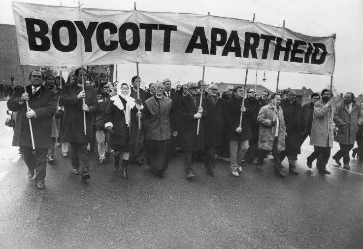People march under a "Boycott Apartheid" banner