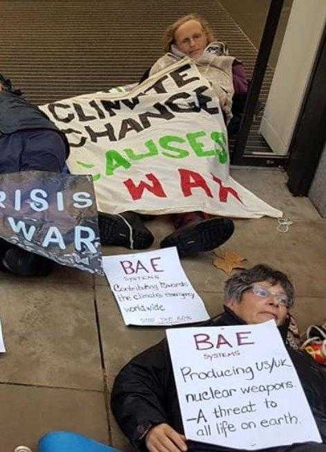 Activists lie on the floor holding banners about climate change and militarism