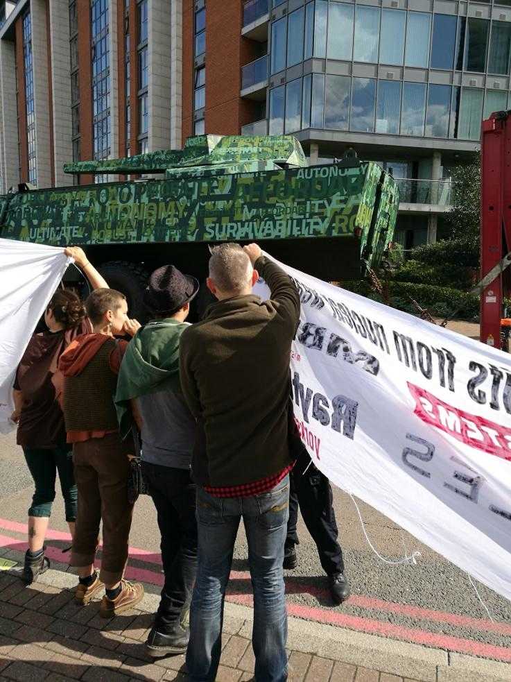 Activists hold banners as a tank drives past in the background