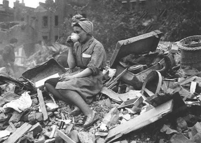 A woman drinks a cup of tea amid a destroyed building. The photo is black and white.