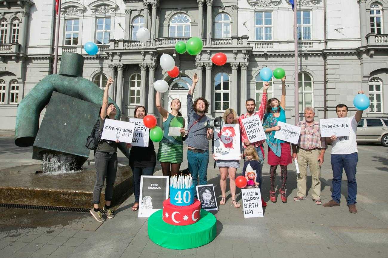 Les gens tenant des ballons et des bannières disant joyeux anniversaire sur une place publique.