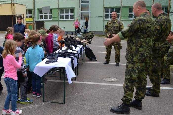 Soldiers talk to young children, who are stood in front of a table covered with guns.