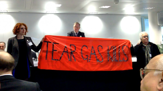 Activists interrupt a shareholder meeting with a banner that reads "Tear Gas Kills"