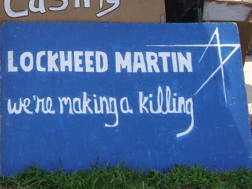 A protest banner mimic the Lockheed Martin logo. The sign reads "Lockheed Martin: we're making a killing"
