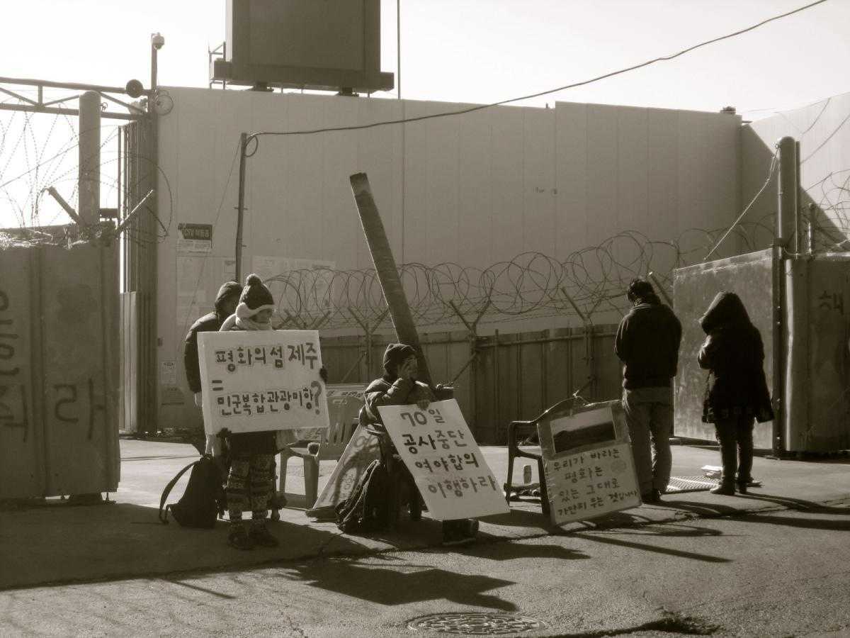 A blockade at Jeju Naval Base - activists stand in front of the gates with signs.