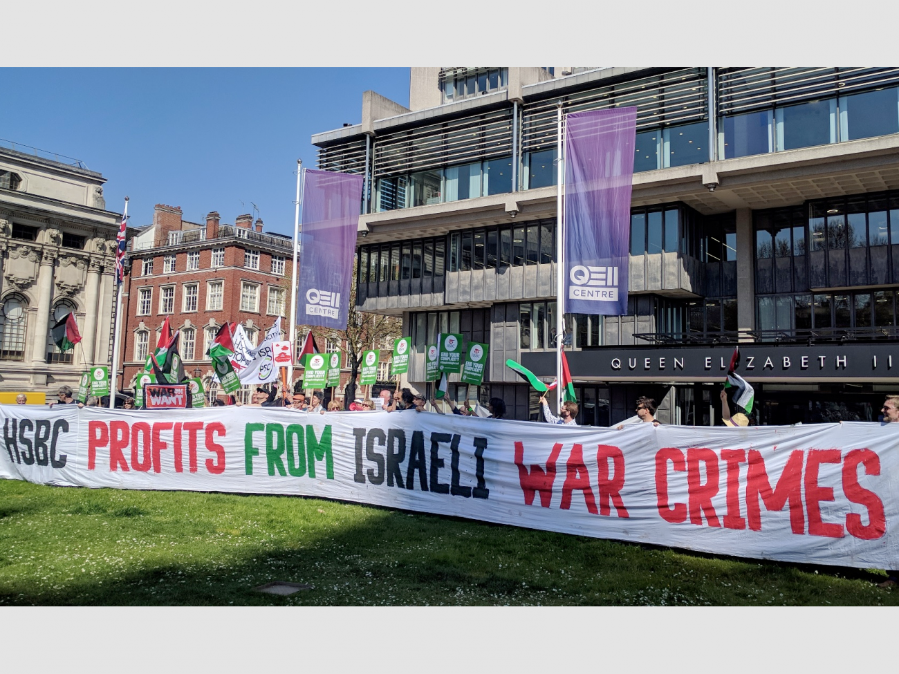 A large group of people stand behind a banner reading "HSBC profits from Israeli war crimes"