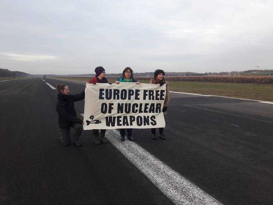 Four activists stand in a runway with a banner reading "Europe free of Nuclear Weapons"