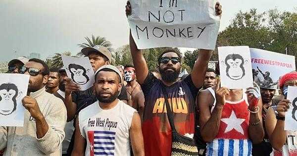 A number of people stand with monkey masks. One holds a sign reading "I'm not a monkey"