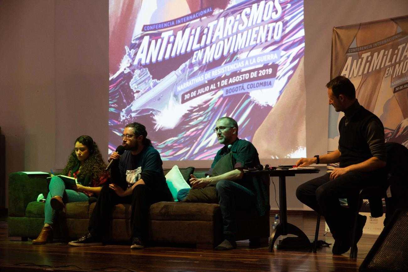 Four people sit in front of a screen with the words "Antimilitarism in Movement"