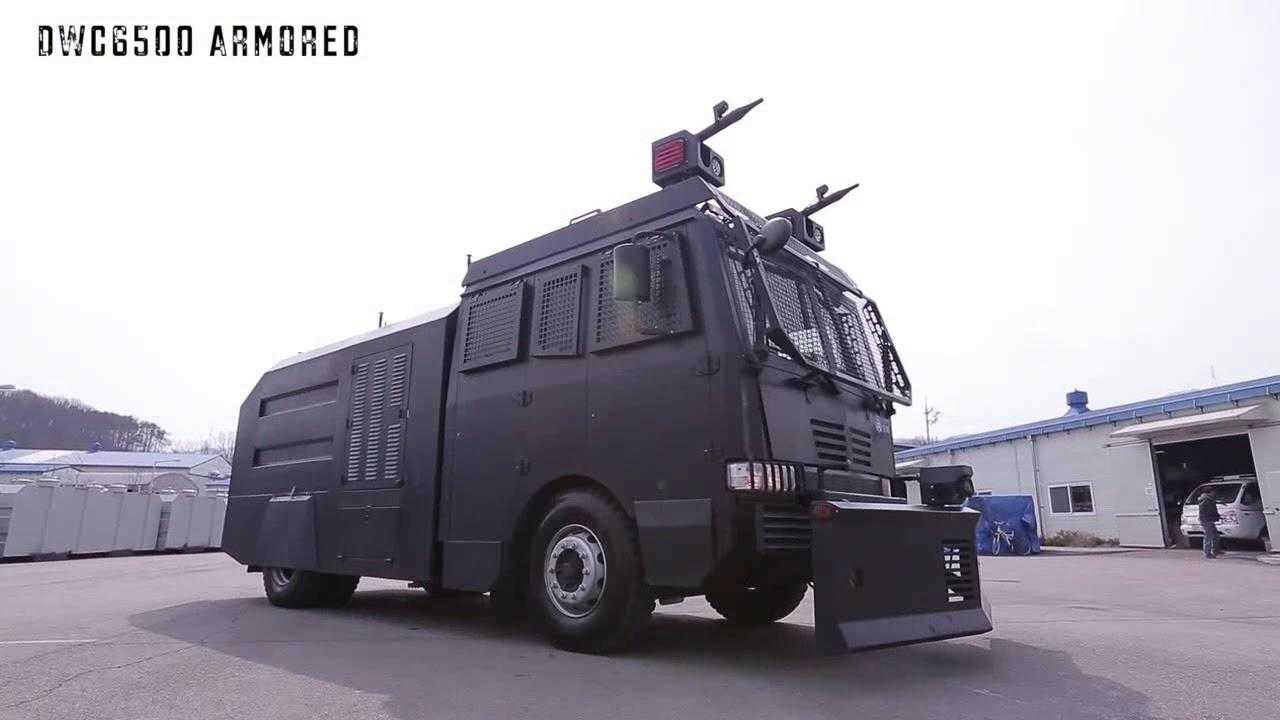 A Daeji water cannon sat parked in a car park. The vehicle is black with shielded windows and two water cannons on top.