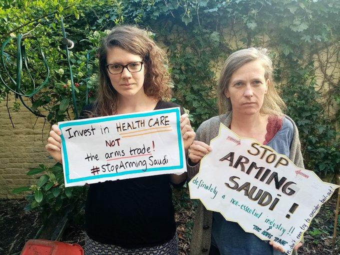 Two people stand holding signs saying "Stop Arming Saudi"