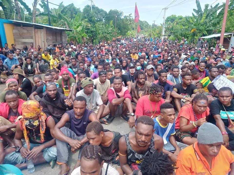 A large crowd of Papuans sit on the ground.