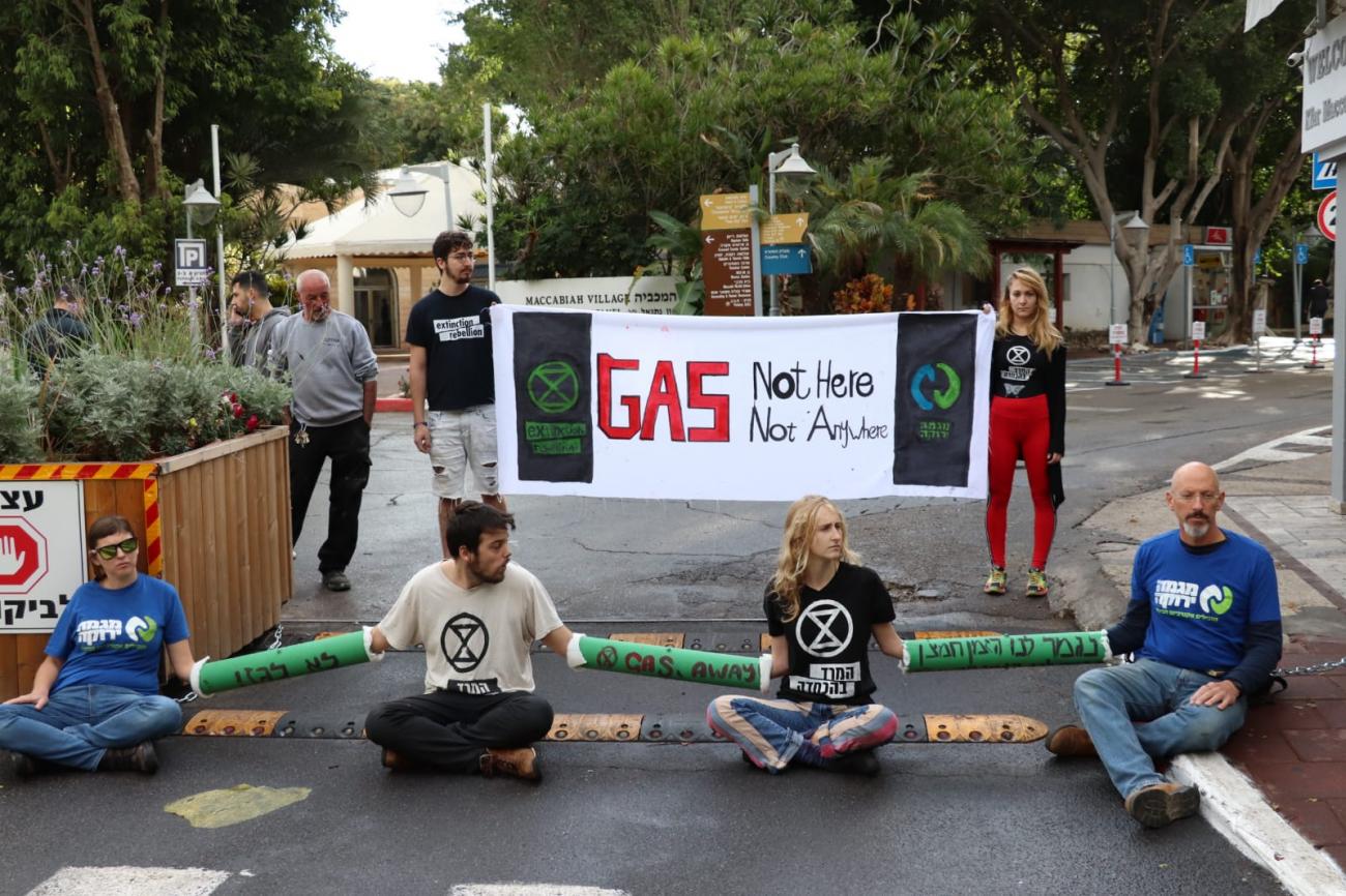 Varios activistas están encerrados juntos al otro lado de la carretera. Detrás, otros dos activistas sostienen una pancarta en la que se lee "Gas: aquí no, en ningún sitio"