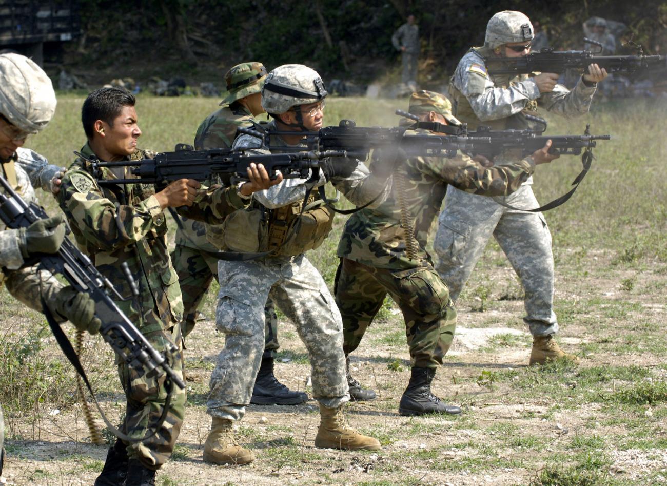 Soldiers from the USA and Mexico stand in a line, firing machine guns