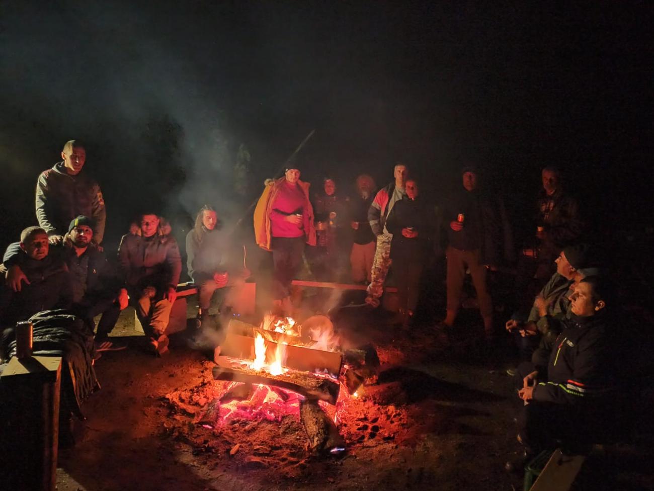 Un gran grupo de personas sentadas alrededor de una hoguera por la noche