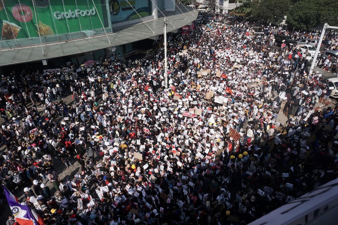 A large crowd of people march down a street. The photograph is taken from above.