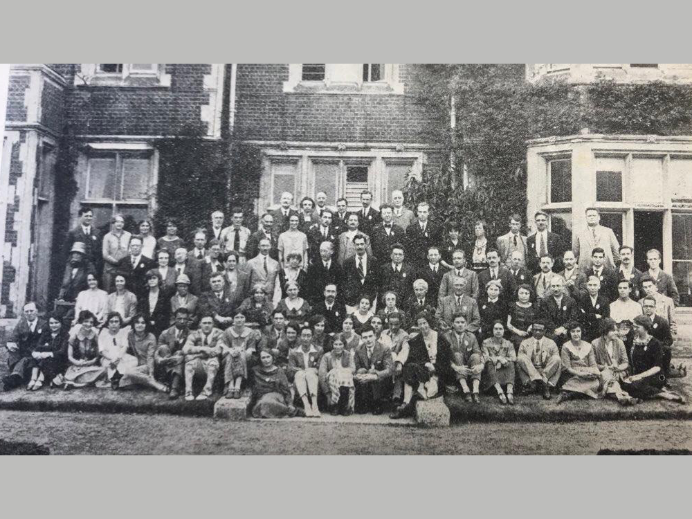 Una foto en blanco y negro que muestra a muchas personas sentadas en el exterior frente a un viejo edificio