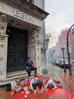 Un hombre vestido como ejecutivo de BBVA de pie sobre un montículo de personas que parecen cadáveres.