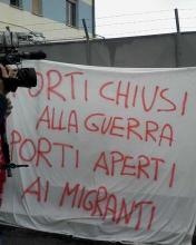 A banner in Italian protests reading "port closed to war, open to migrants"