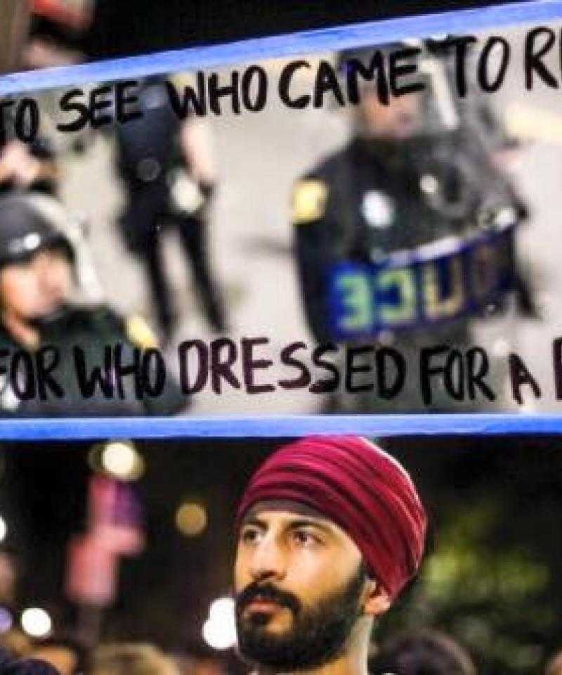 A man holds a mirror to the police, on which is written "Who came dressed for a riot?"
