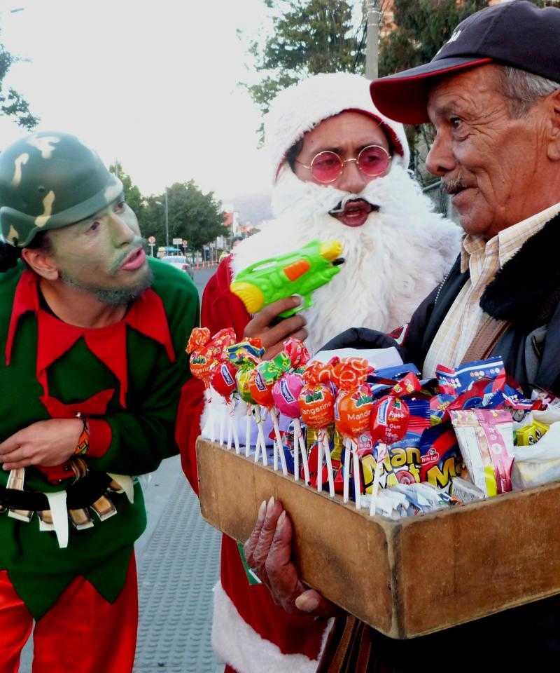 Activistas antimilitaristas entrevistan a miembros del público disfrazados de santa y elfos navideños, armados con pistolas de agua y cascos militares