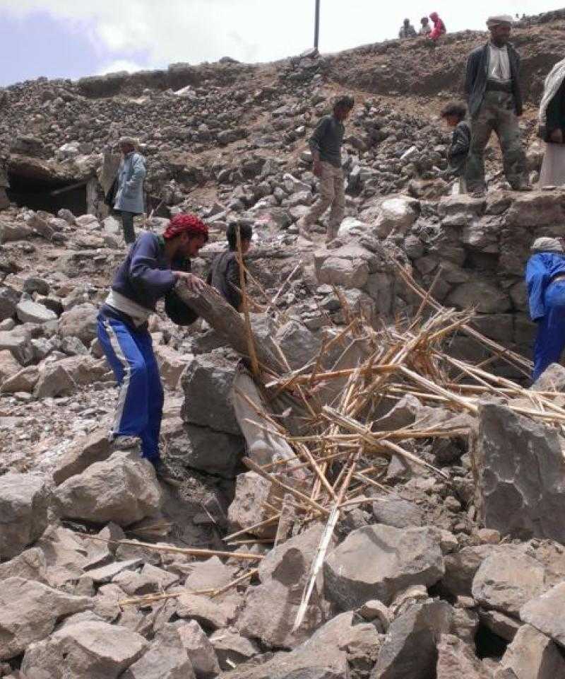Around a dozen people climb over the rubble of demolished buildings in Yemen.