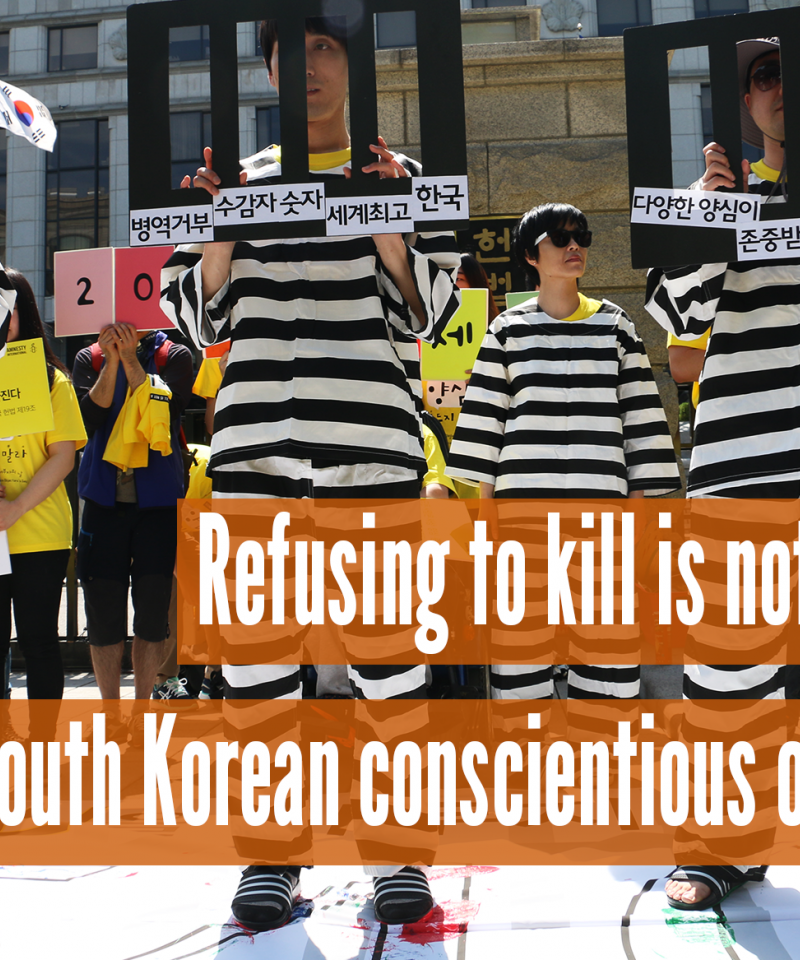 Las personas de pie con carteles que parecen barrotes de la prisión, con el texto "Negarse a matar no es un delito, objetores de conciencia surcoreanos libres"