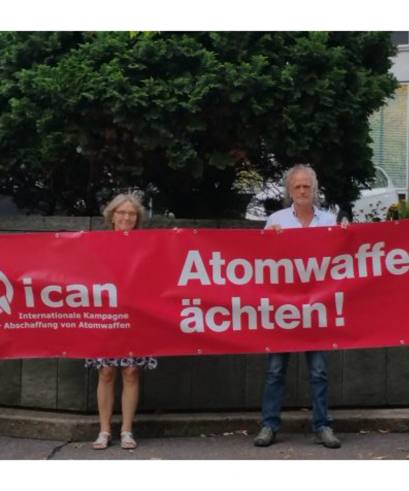 Four people stand with a red banner reading "Ban Nuclear Weapons" 