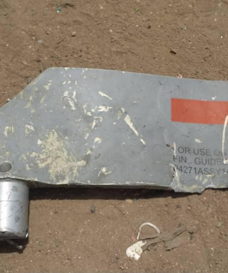A piece of metal marked with identification numbers lies on sandy ground