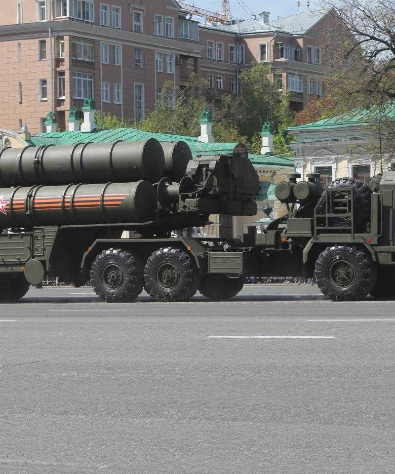 A large truck pulls an even larger trailer. On the trailer are several large missile launchers. Everything is painted dark khaki green