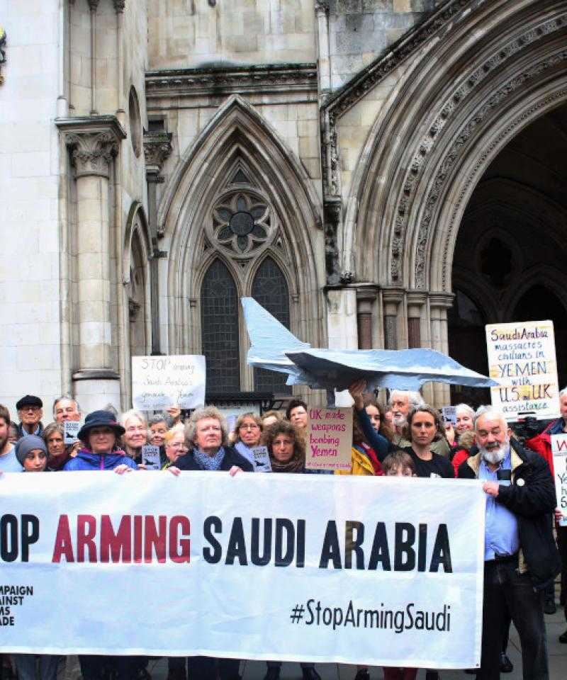 A large crowd stand in front of the royal courts of justice. They are holding a banner with the words "Stop arming Saudi Arabia"