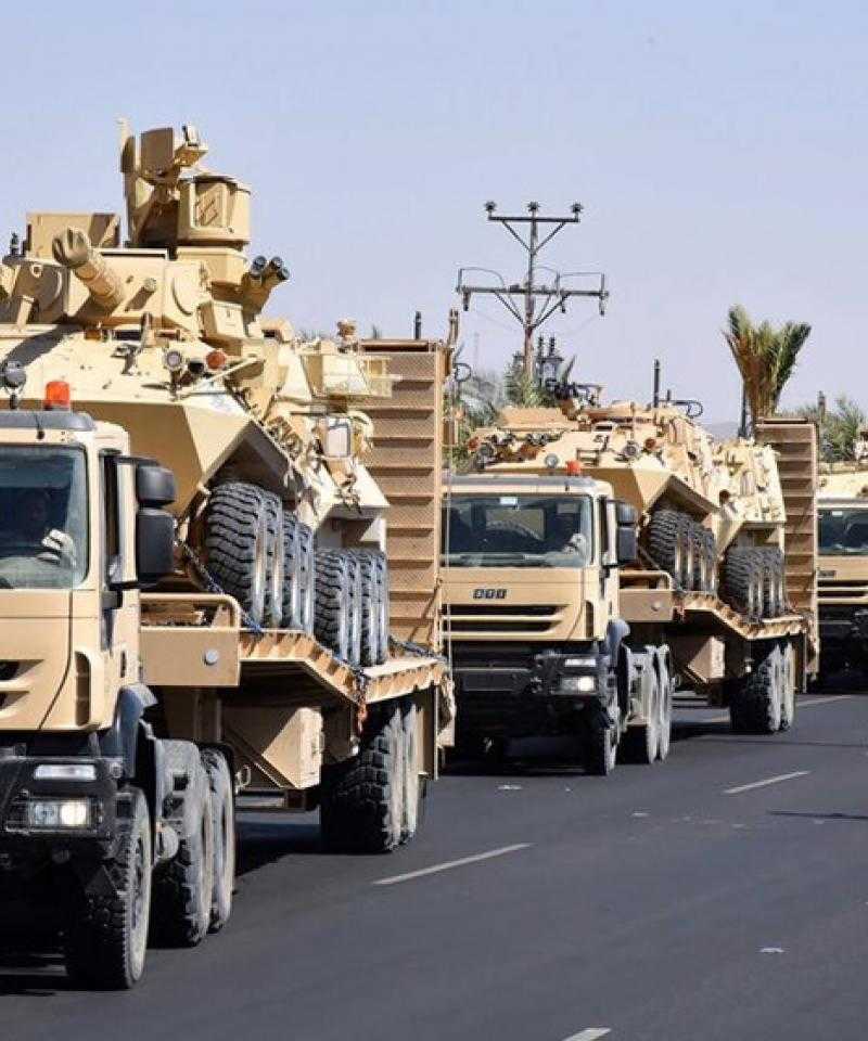 The image shows a line of heavy trucks carrying armoured vehicles.