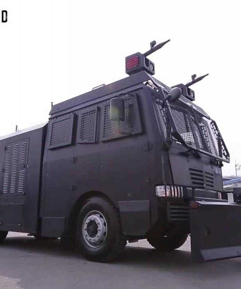 A Daeji water cannon sat parked in a car park. The vehicle is black with shielded windows and two water cannons on top.