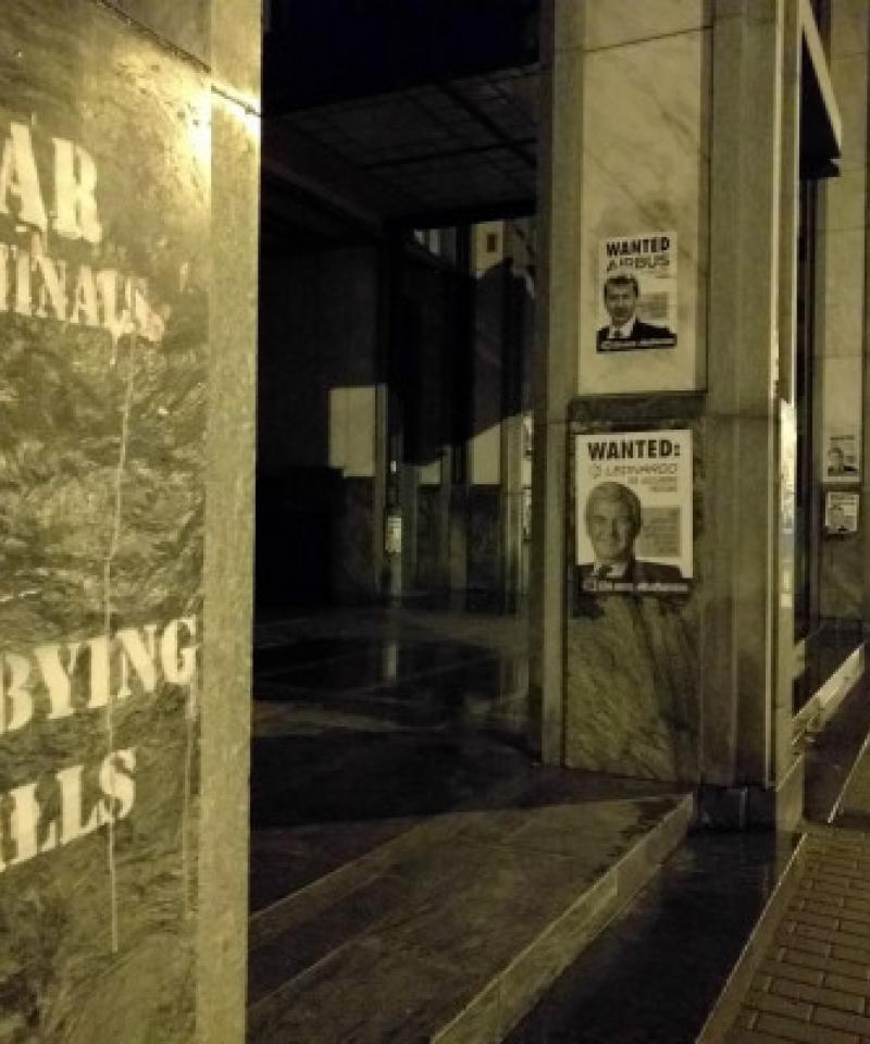 Image taken at night. Grafitti saying "Lobbying kills" and "war criminals" alongside a Wanted poster