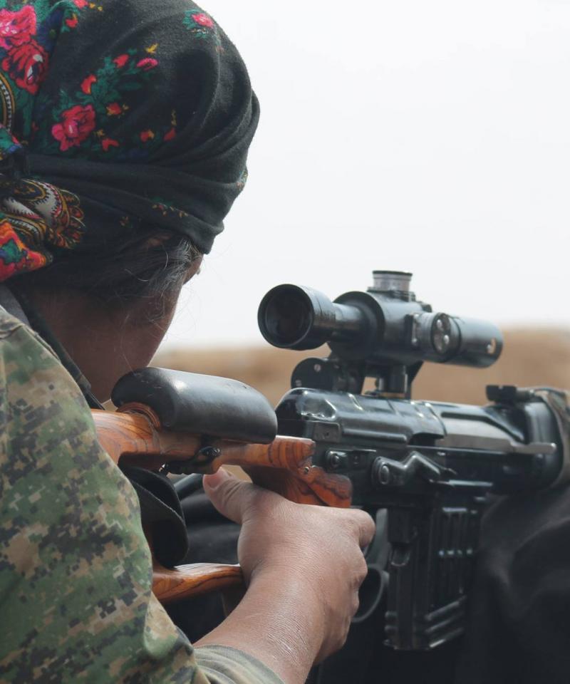 A woman with her back to the camera aims down a rifle