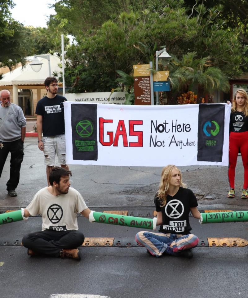 A number of activists are locked together across the road. Behind stand two other activists holding a banner reading "Gas: Not here not anywhere"