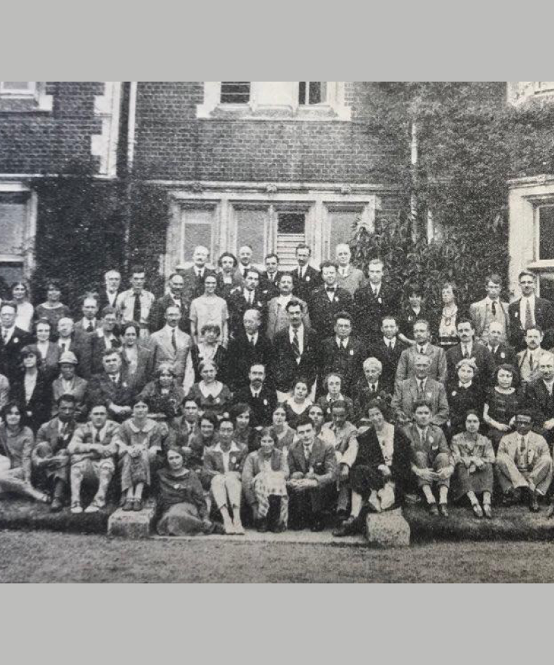 A black and white photo showing many people sat outside in front of an old building