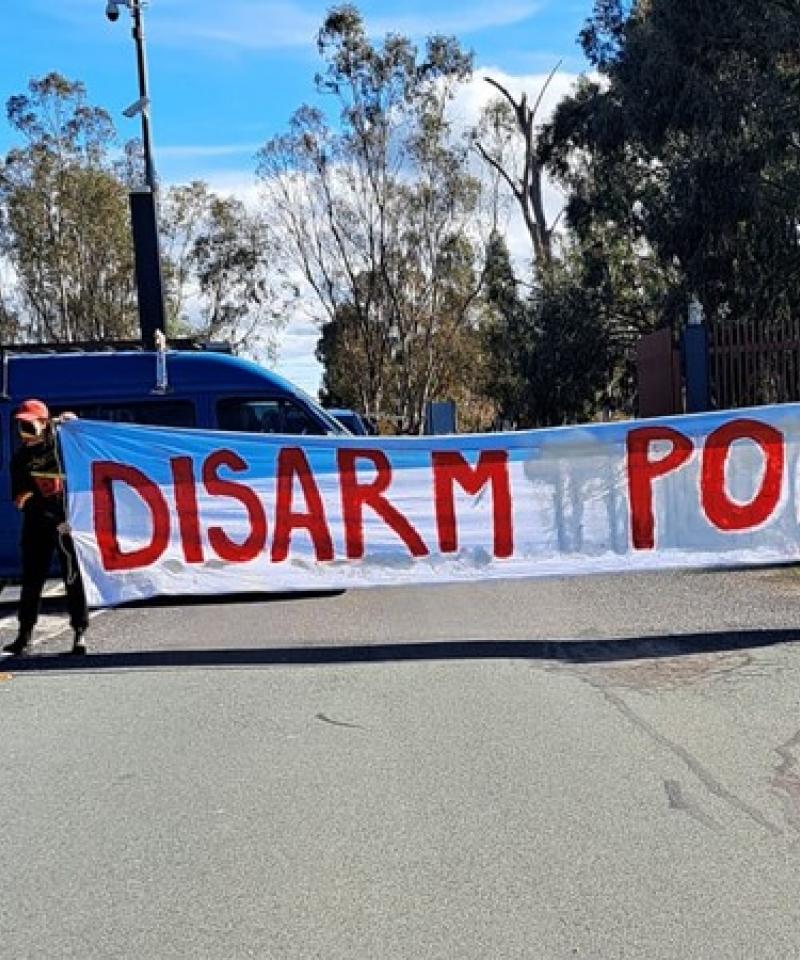 Two activists hold a large white banner reading "disarm police"