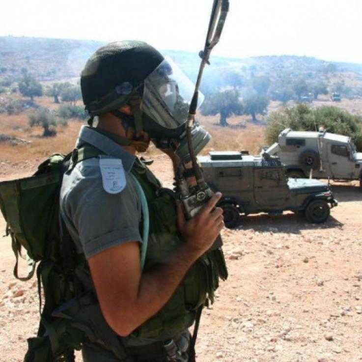 A member of Israel's Border Police wearing a gas mask. There are several armoured vehicles parked in the background.