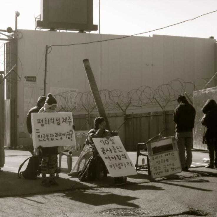A blockade at Jeju Naval Base - activists stand in front of the gates with signs.