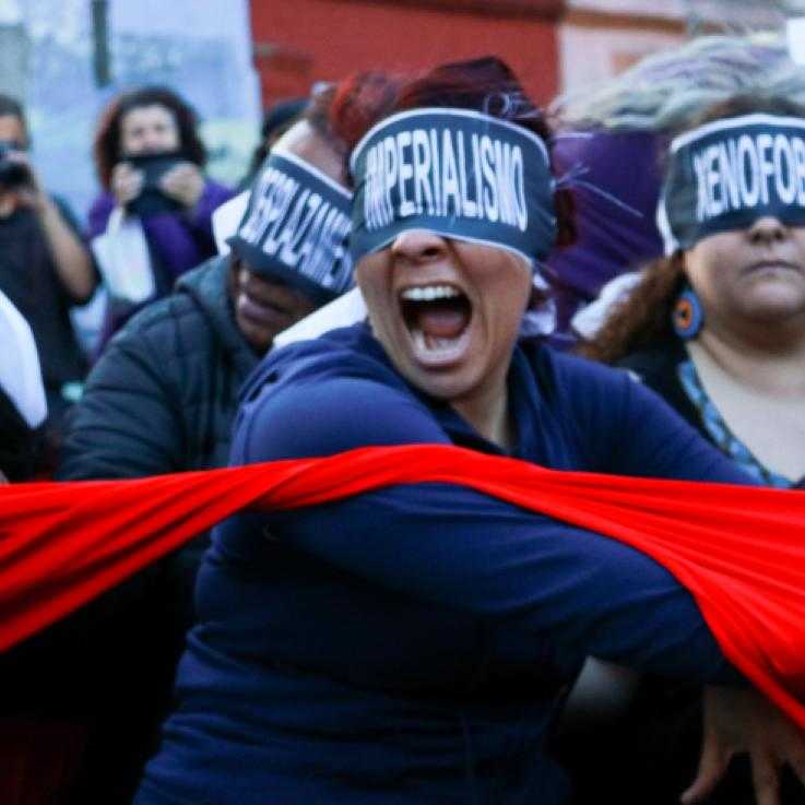 A protest. A woman in the fore ground is asked wit h the word "imperialism". She is throwing a red cloth. Behind her are other masked protesters.