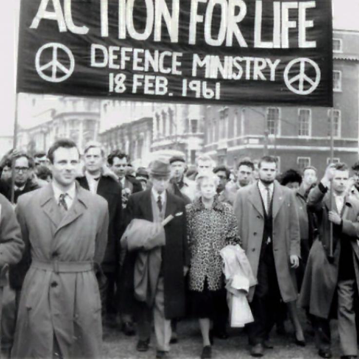 A black and white photo depicting a crowd of people carrying a banner reading "Action for Life"